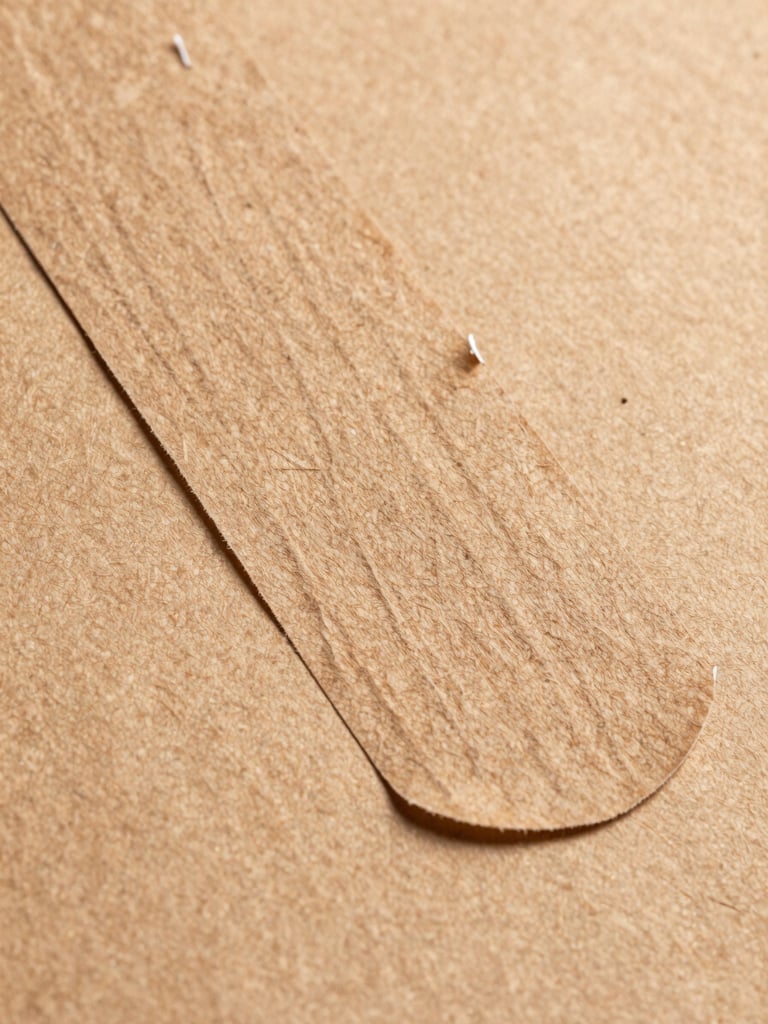 Extreme close-up of a kraft paper mailer adhesive strip being peeled, revealing the permanent seal layer, kraft weave texture sharp in foreground under flat north-facing studio overhead light, brown paper grain filling the frame edge-to-edge