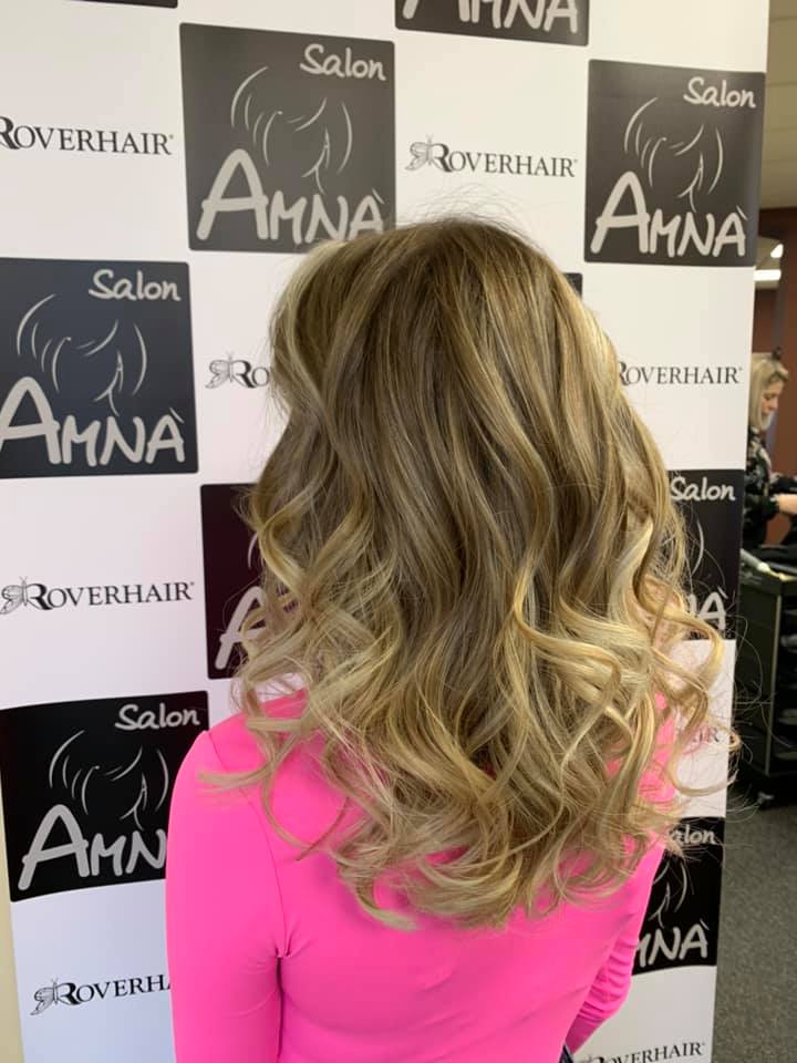 Woman with long blonde wavy hair highlighting professional hair color services at Salon Amna.