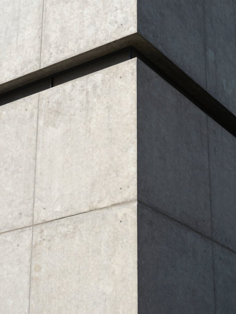 Sharp architectural angle of a modern concrete building facade, crisp daylight shadows, minimalist composition.