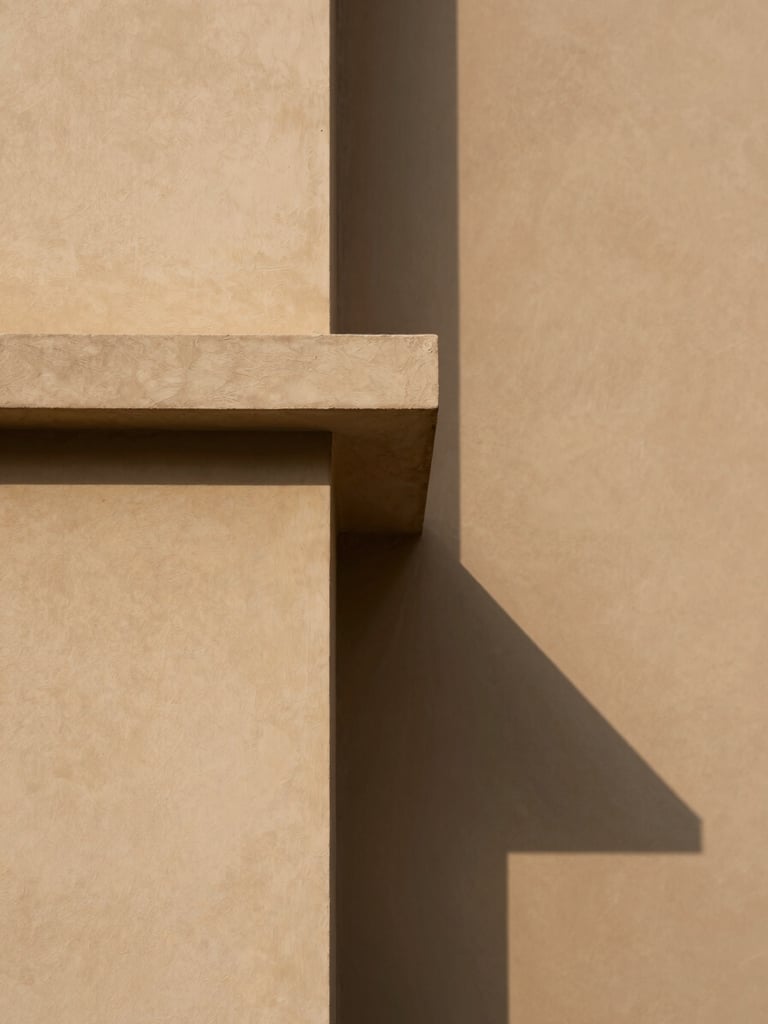 A clean, minimalist architectural detail showing sharp lines of light and shadow on a warm sand-colored plaster wall, representing balance and order