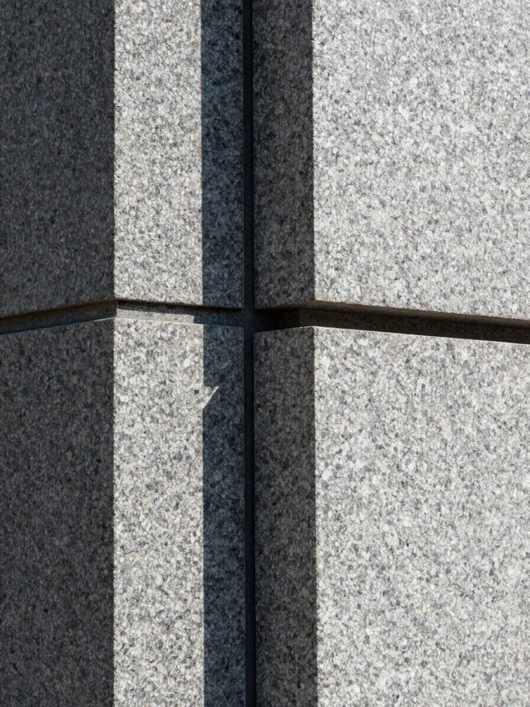 Abstract architectural close-up of heavy granite blocks meeting with absolute precision, sharp shadow lines, cool natural light.