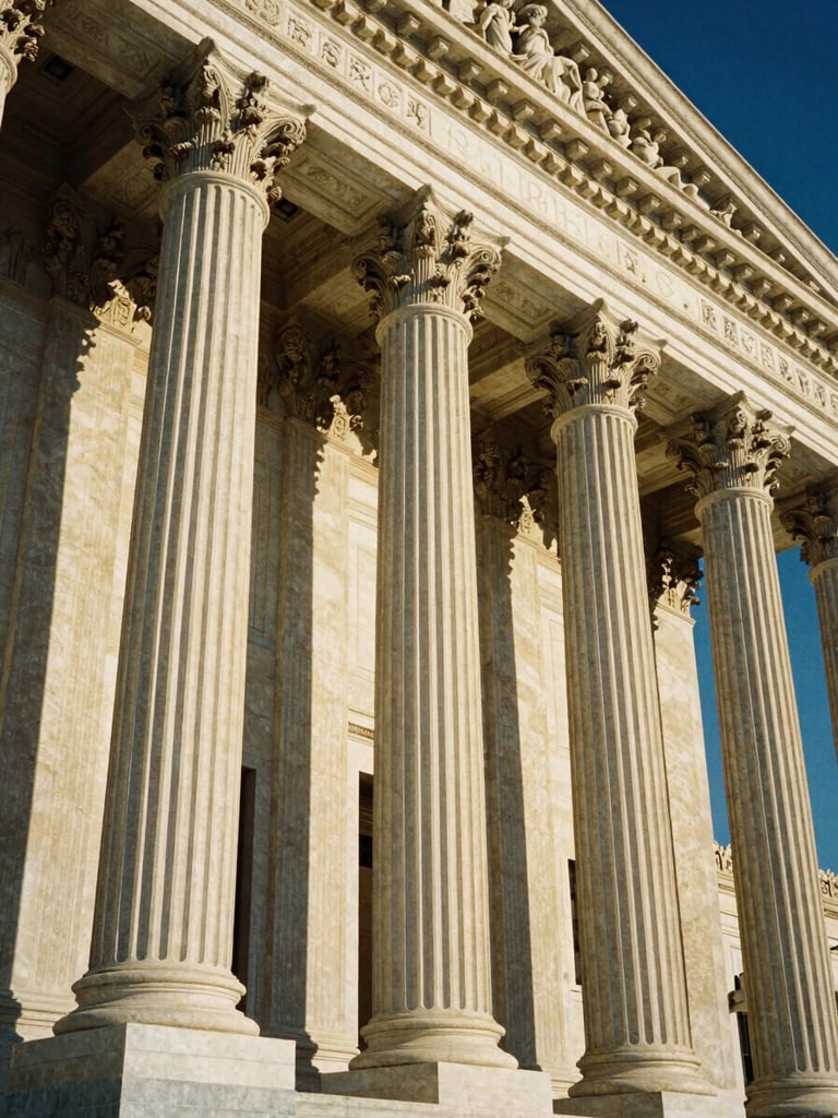 Low-angle heroic shot of the US Supreme Court building columns, sharp architectural details, dramatic golden-hour sunlight casting deep shadows, 35mm