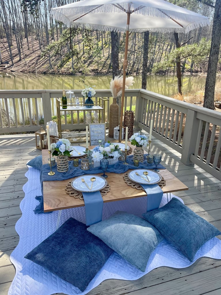 Blue luxury picnic by Gathered Grace Picnic Co with bar cart, umbrella, plush pillow floor seating