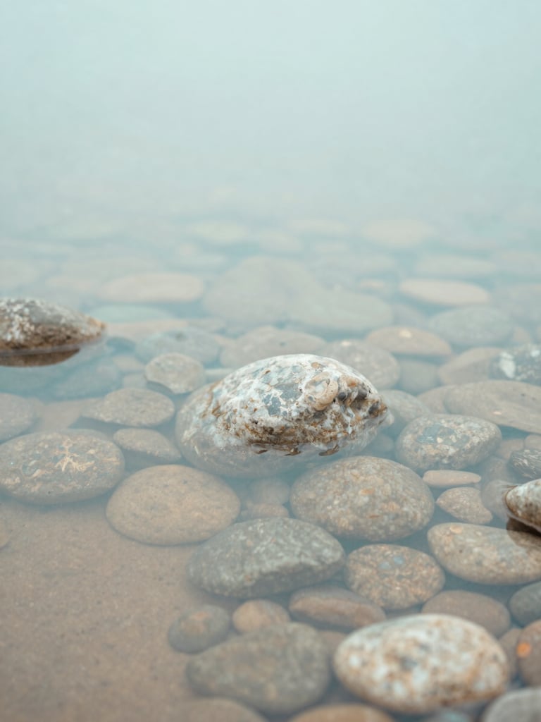 Soft close-up of smooth river stones in shallow clear flowing water, diffused overcast daylight, calming turquoise tones, 35mm