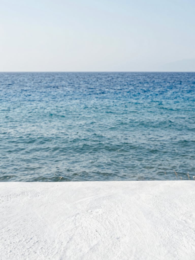 Minimalist coastal horizon of the Aegean sea, soft water movement, clean bright daylight, whitewashed plaster texture in the foreground, serene and restorative atmosphere.