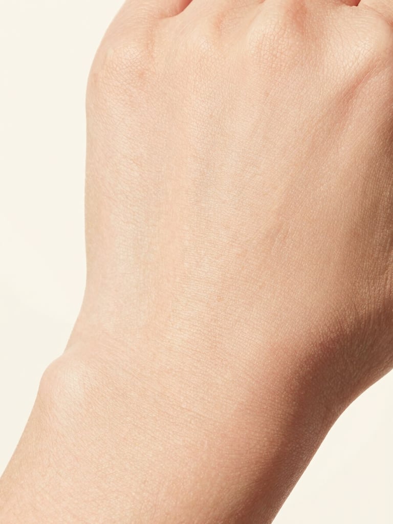 Ultra-close macro shot of clean, unretouched skin texture showing real natural glow, high-key studio lighting, soft cream background