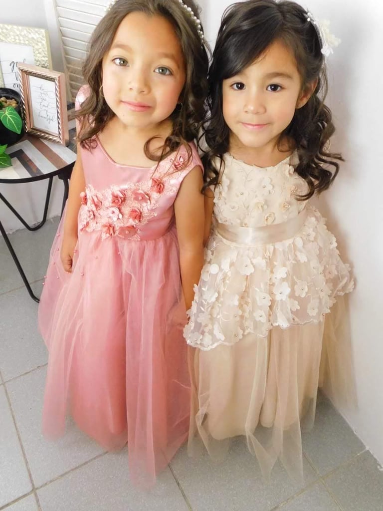 Dos niñas paje luciendo elegantes vestidos de tul en tonos rosa y crema, con aplicaciones florales,
