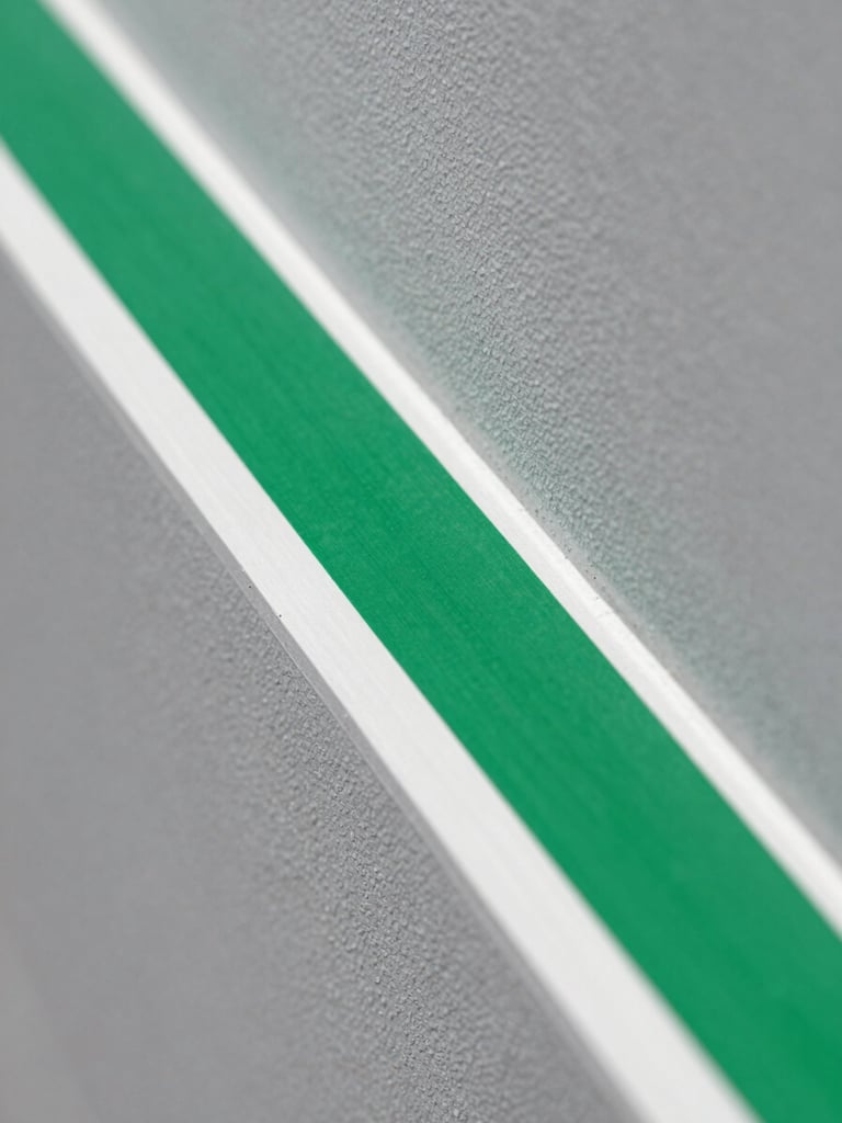 Macro close-up of a laser-straight green painter's tape line being peeled from a crisp slate grey wall, revealing a flawless stark white trim edge under bright daylight.