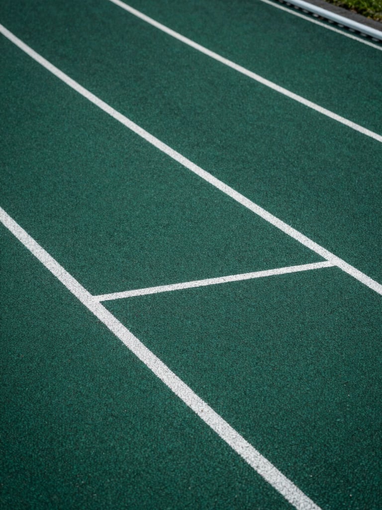 Close-up overhead view of a running track's lane markings on rubberized surface, crisp geometric lines in deep forest green and white against charcoal base, studio-controlled cool light emphasizing material texture and spatial precision, no human presence