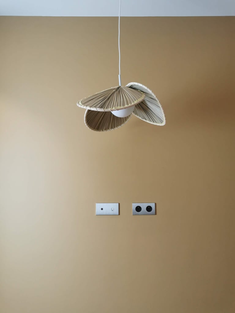 Modern woven rattan pendant light hanging against a warm beige wall with minimalist silver outlets.