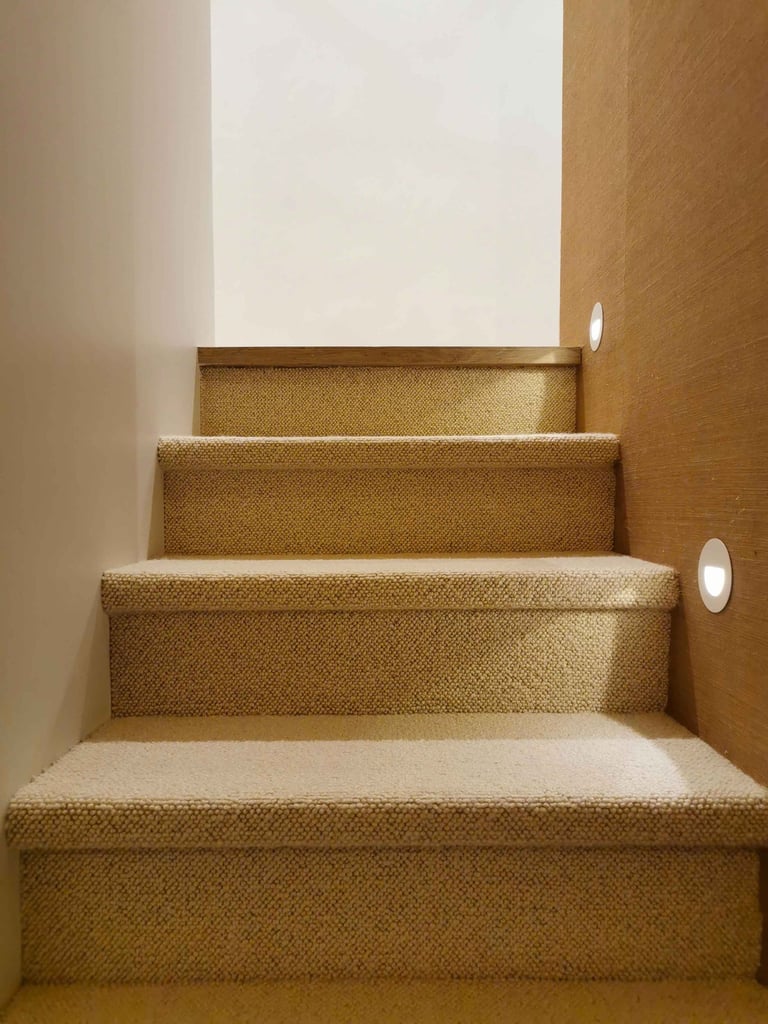 Modern indoor staircase with beige carpet runner and round LED recessed wall lights.