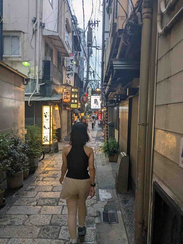 Woman walking through a narrow food street lined with restaurants and lanterns in Osaka, Japan.