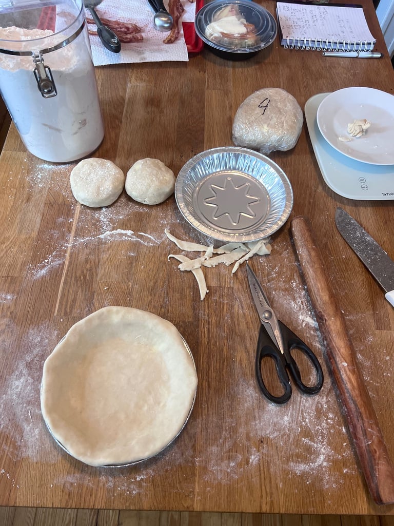 Homemade pie dough preparation on a wooden table with a rolling pin, flour, and baking tins.