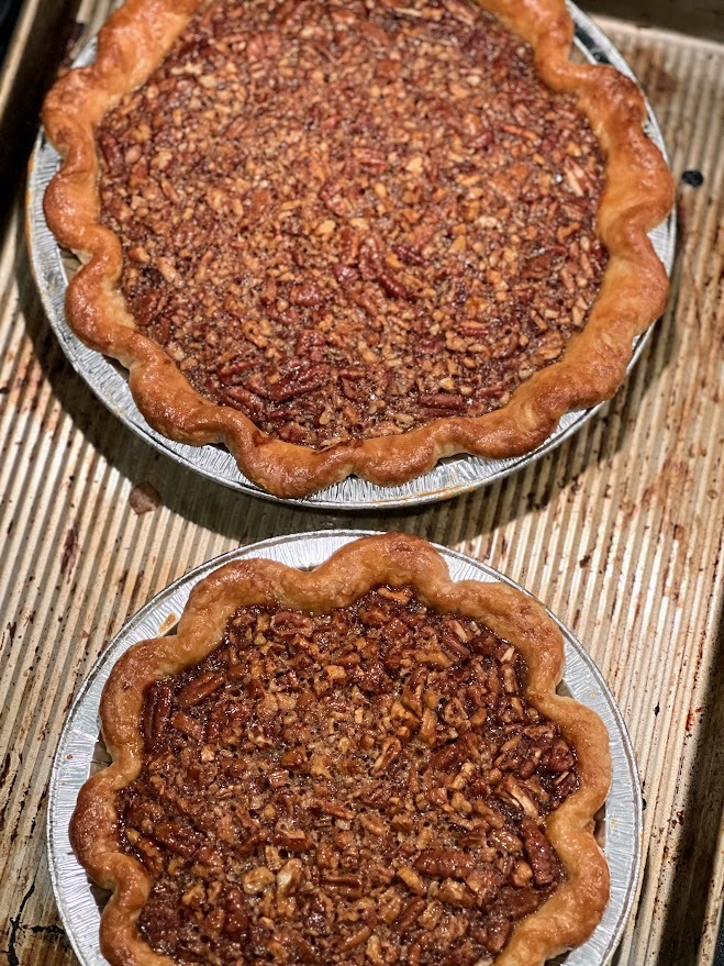 Two freshly baked pecan pies with golden fluted crusts sitting on a metal baking sheet.