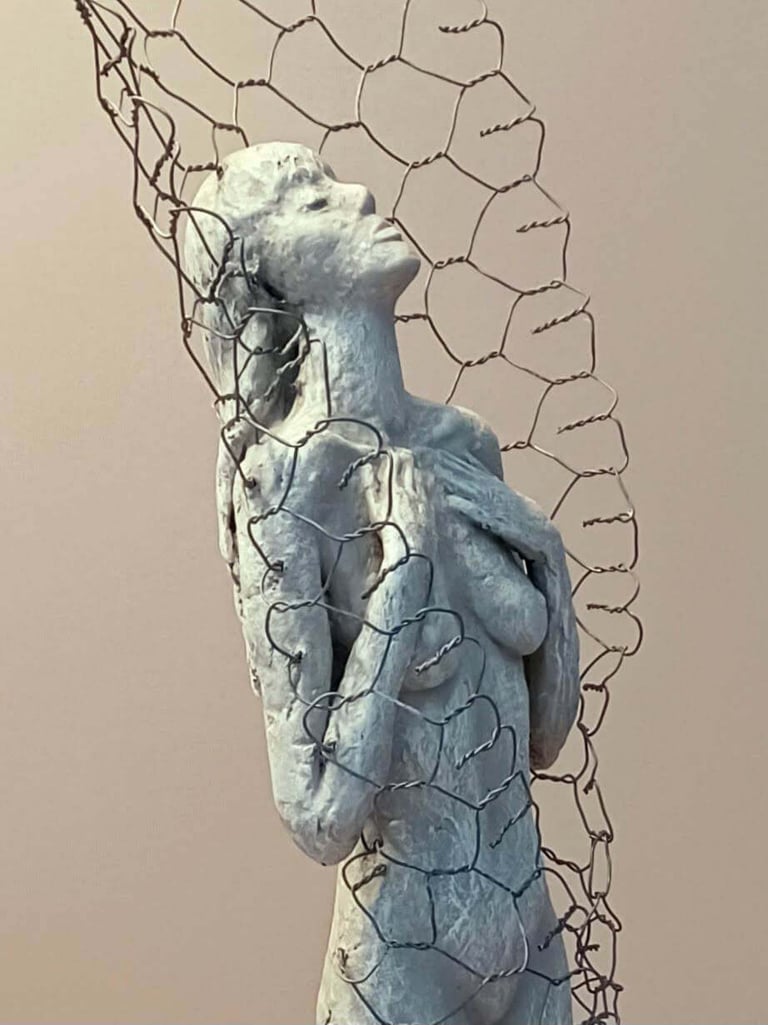 Close up of a female figure, leaning back with eyes closed, surrounded by a wire netting enclosure