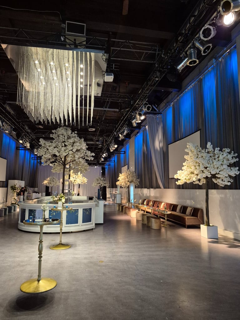 Luxury event venue featuring blue up lighting, white blossom décor, and a circular bar