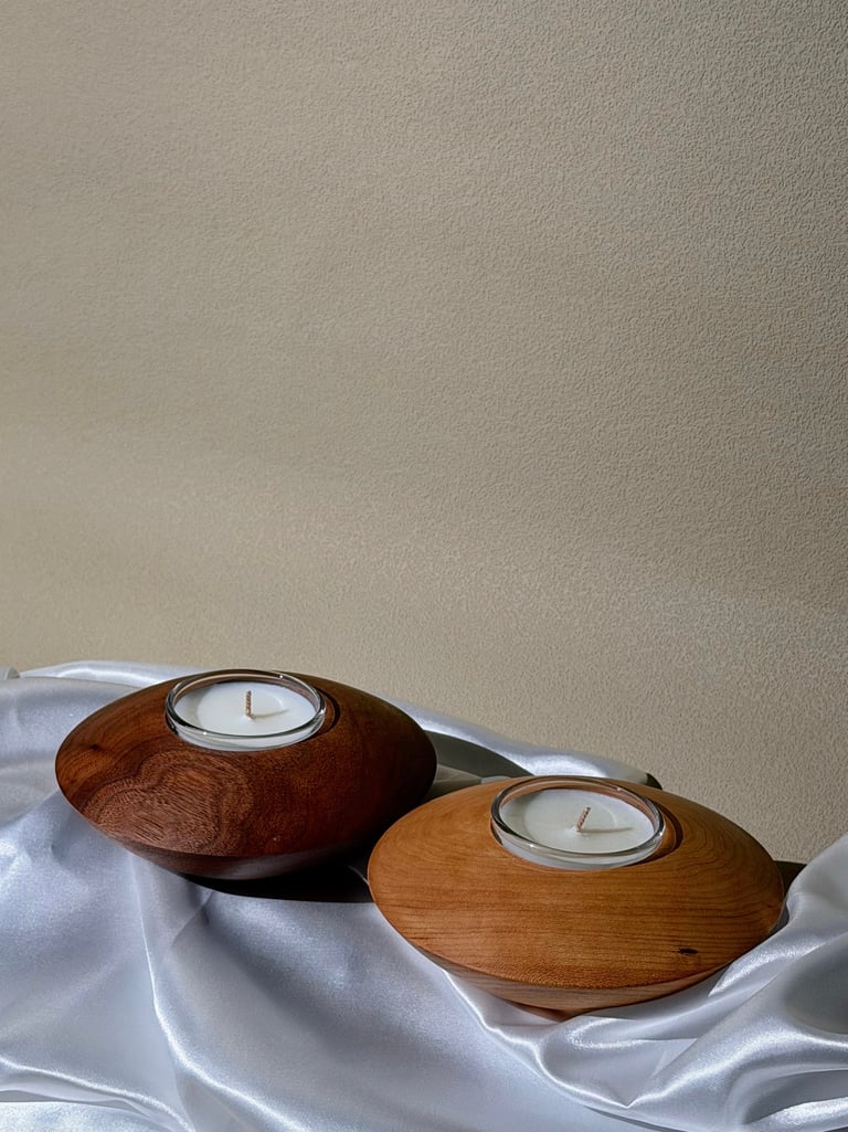Two round wooden tea light candle holders on white silk fabric against a textured wall.