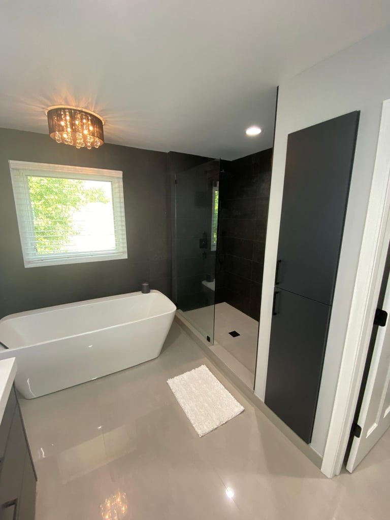Modern master bathroom featuring a white freestanding bathtub and a glass walk-in shower with dark tiles.