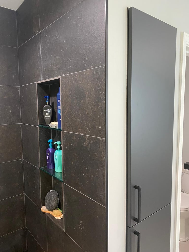 Modern bathroom shower with dark large-format tiles and a recessed wall niche with glass shelves for toiletries.