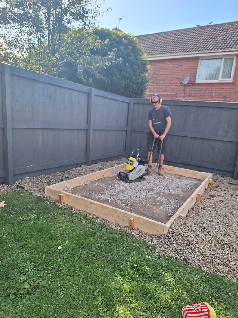 a man compacting a base for a shed
