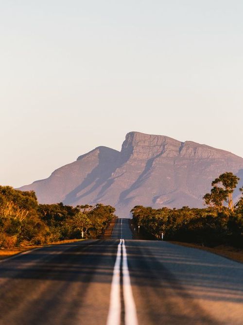 Empty asphalt road leading toward a massive mountain range during a golden hour sunset.
