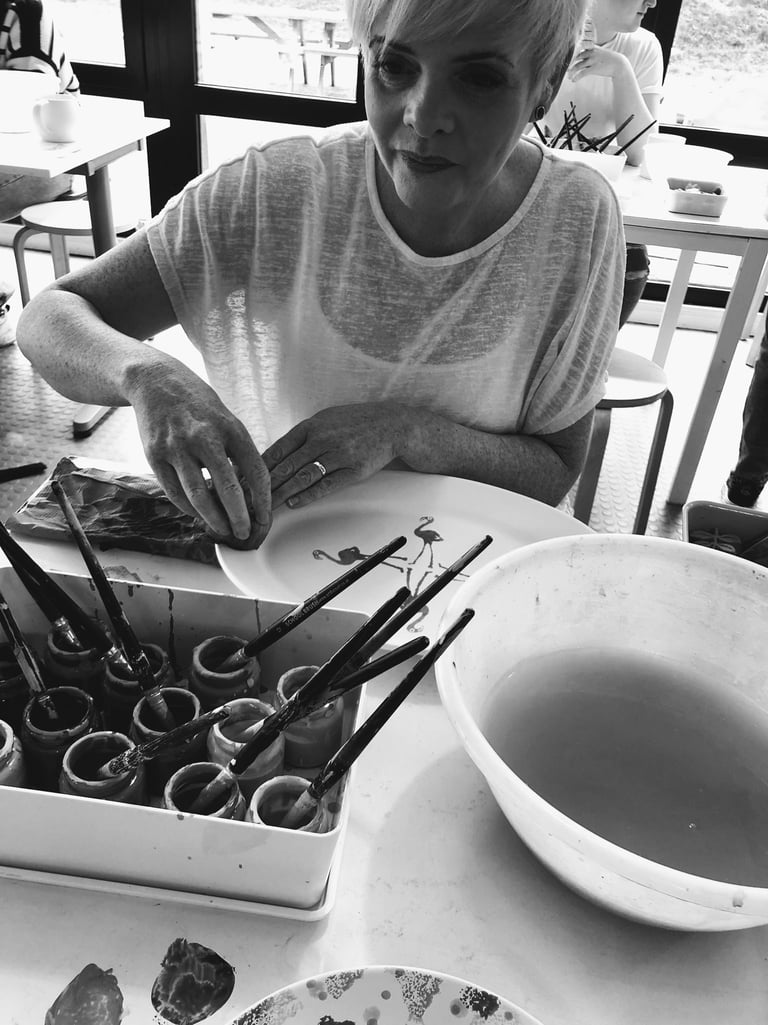 Patricia Madden Artist paints a ceramic plate with flamingo designs in a pottery studio workshop.