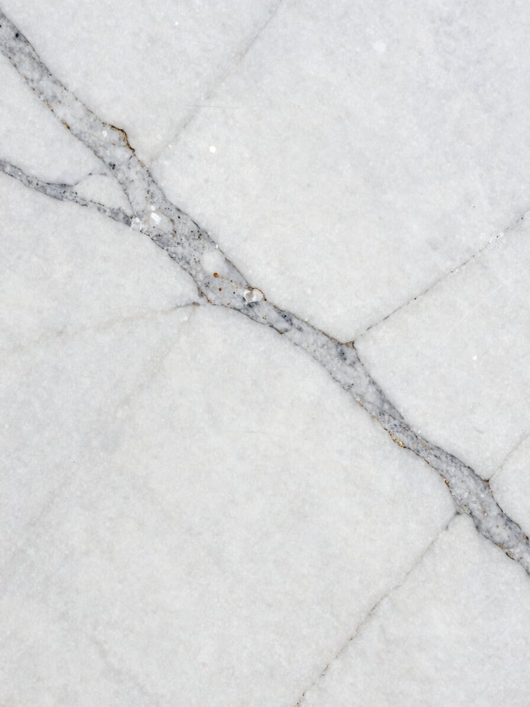 Extreme close-up of Statuario marble slab under north-facing daylight, bold grey veins cutting across pure white stone surface, photographed three inches from surface to reveal crystalline texture, no props