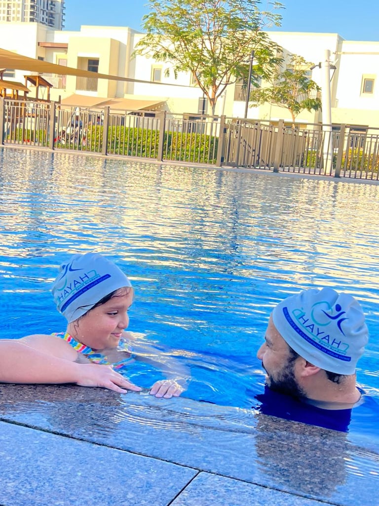 A young girl receives a private swimming lesson from an instructor in an outdoor pool.