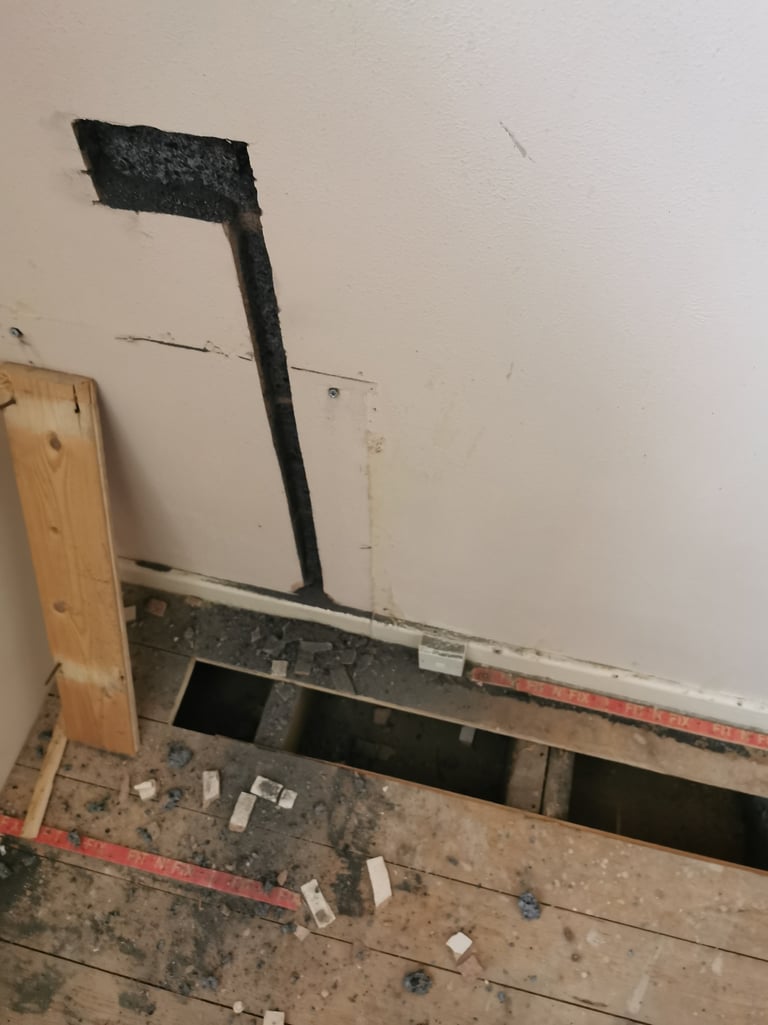 Wall cutout for electrical wiring above removed wooden floorboards.