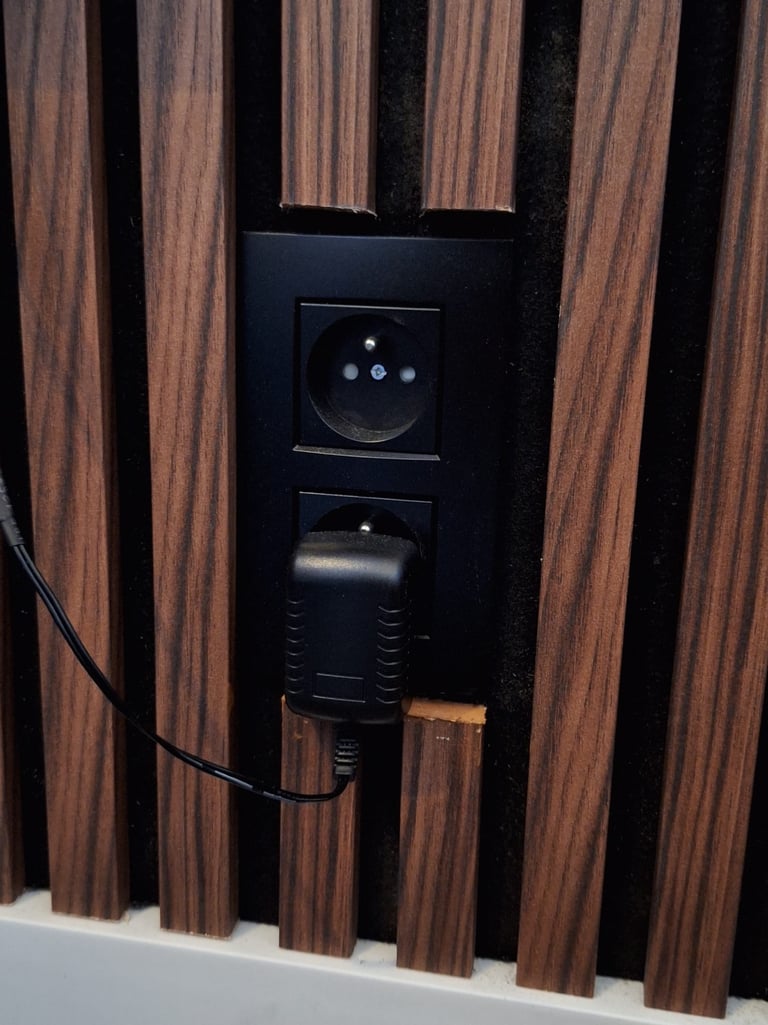 Zoom sur l'intégration de prises noires dans un panneau en lattes de bois foncé