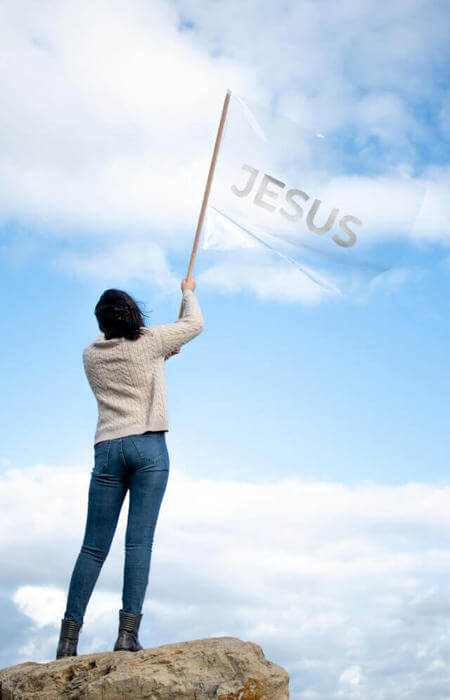 a woman holding a jesus flag on a rock