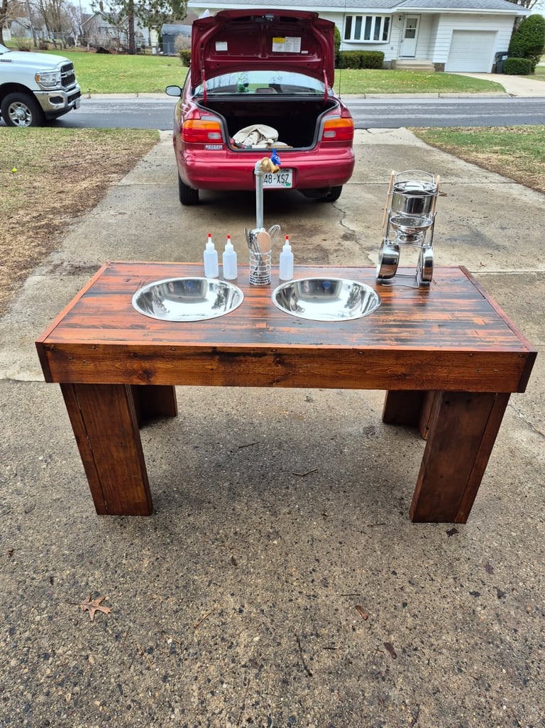 Handmade outdoor wooden mud kitchen for kids with double stainless steel sinks and play utensils.