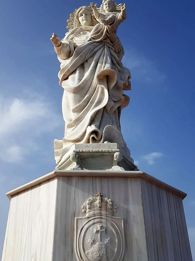 White marble statue of the Virgin Mary holding baby Jesus against a clear blue sky background.
