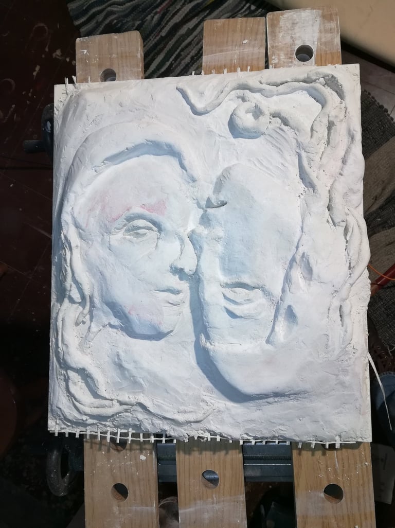 White plaster relief sculpture of two faces in profile on a wooden easel stand.