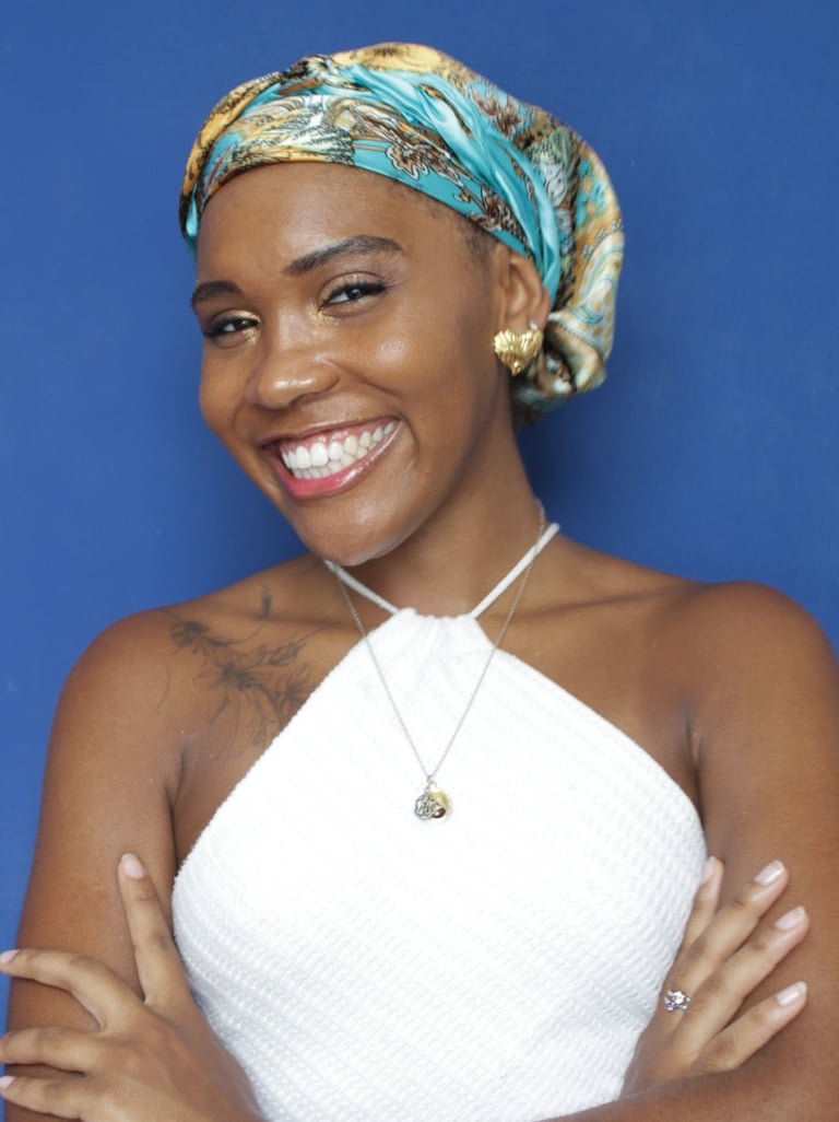 Mulher preta retinta, de semblante alegre e sorriso aberto. Usa lenço na cabeça e brinco dourado.