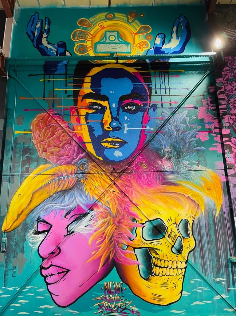 une fresque avec un crâne, une tête violette, deux tête d'oiseau colorés, deux mains et une tête colorée de façe