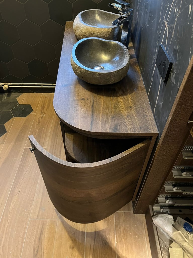 Modern bathroom vanity with double stone vessel sinks and a curved dark wood cabinet.
