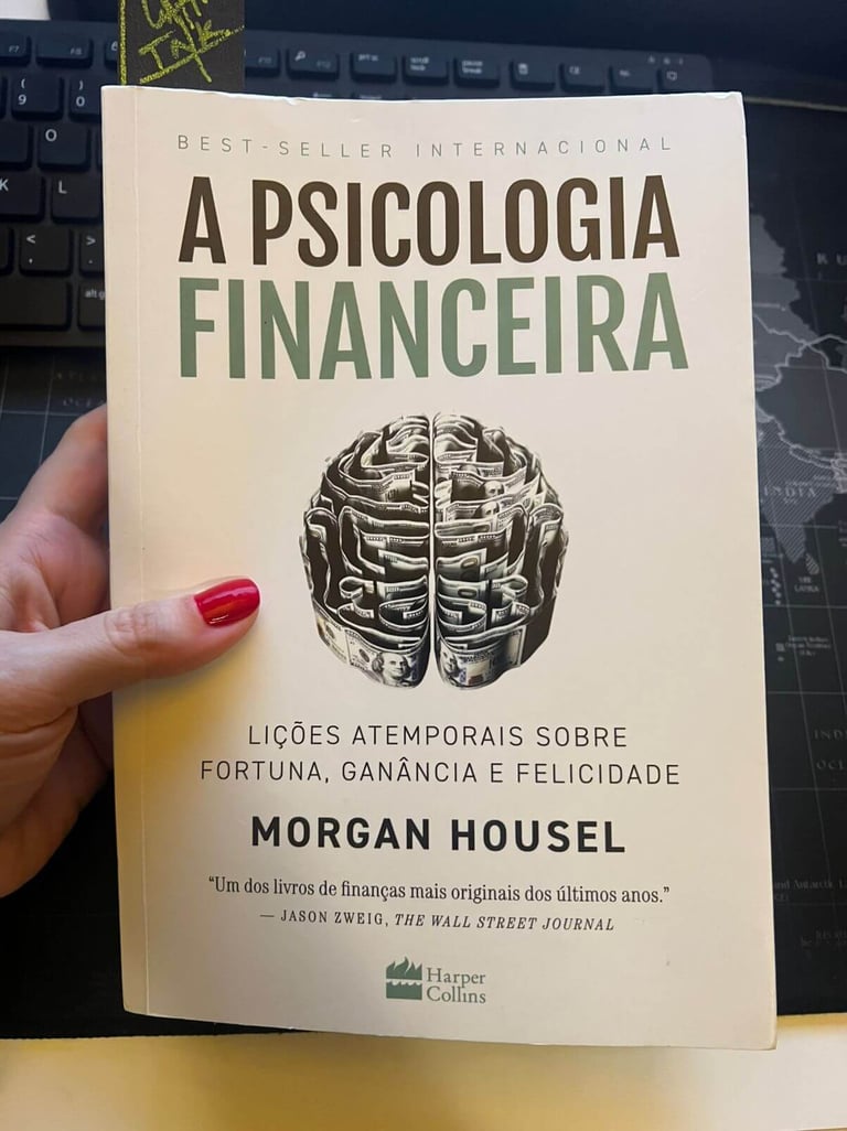 Hand holding A Psicologia Financeira book by Morgan Housel with brain shaped from money on the cover.