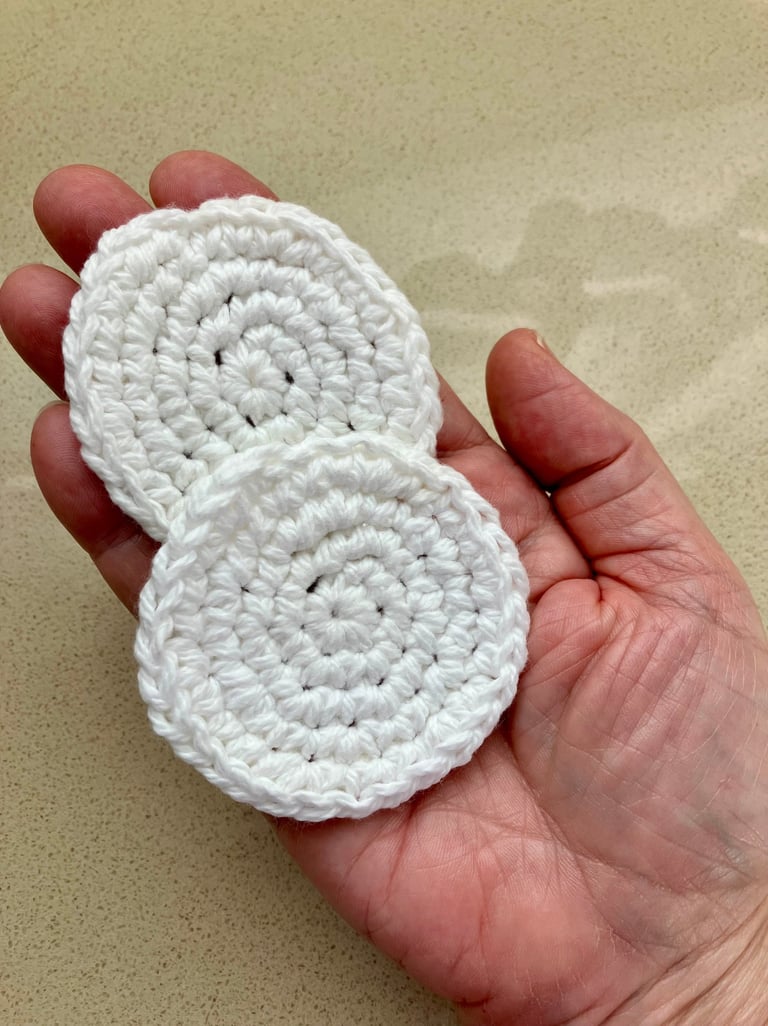 Hand holding 2 small, crocheted, white, round, face scrubbies