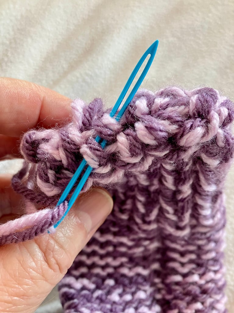 Close-up of yarn needle sewing together end of knitted toe of purple slipper