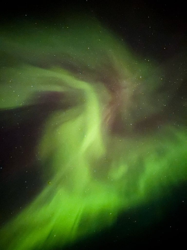 Close-up view of vivid green and purple Northern Lights swirling across a star-filled night sky in the Faroe Islands