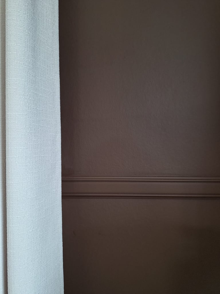 Zoom sur un mur brun avec une moulure et une tenture en lin beige