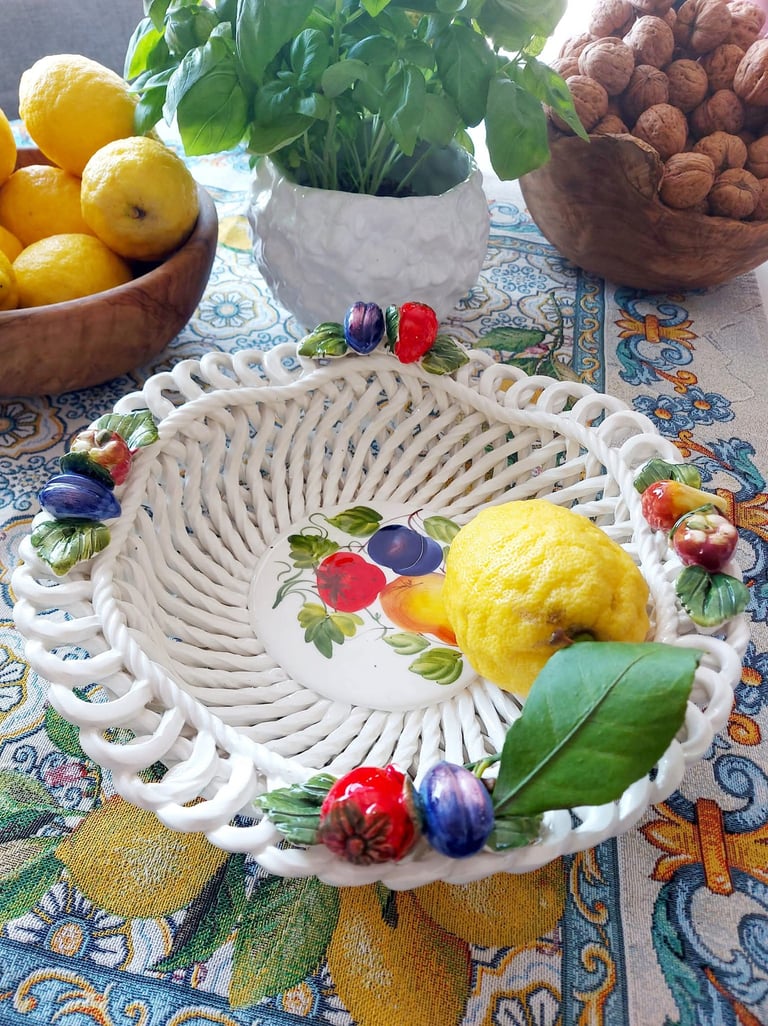 Hand-painted ceramic woven fruit bowl with a lemon on a patterned tablecloth.