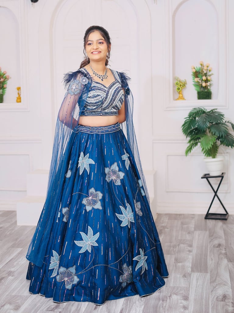 “A bride standing in a bright white studio, wearing a royal blue floral embroidered lehenga with 