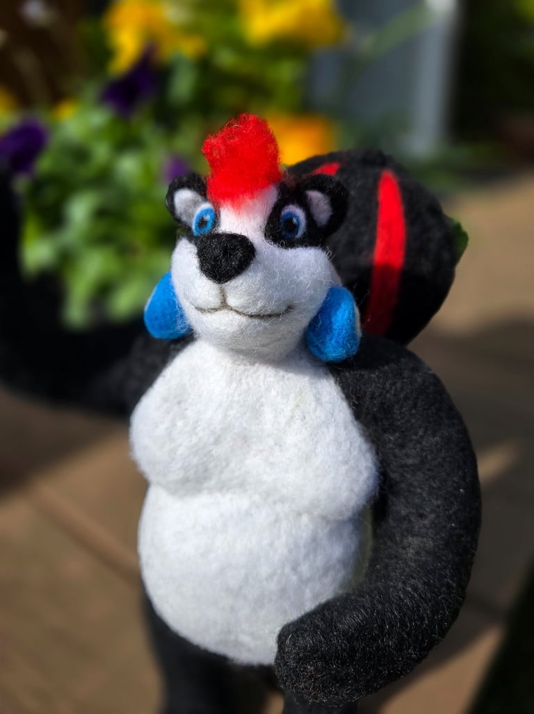 Handmade needle felted skunk figurine with a red mohawk and blue earrings in a garden setting.