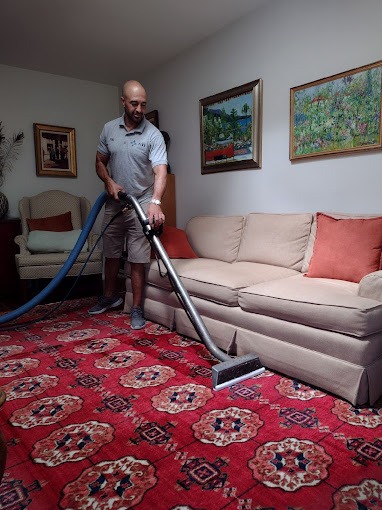 Professional carpet cleaner using a steam vacuum on a red oriental area rug in a living room.