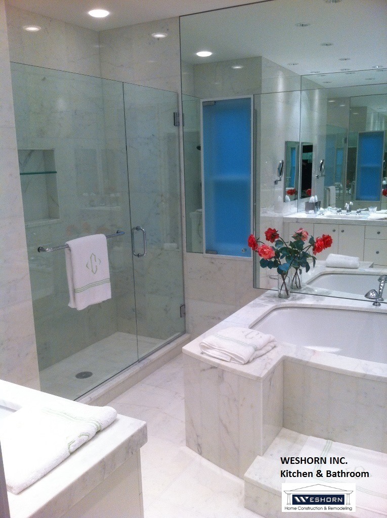 Modern luxury bathroom remodel featuring a glass walk-in shower, marble bathtub, and large vanity mirrors.