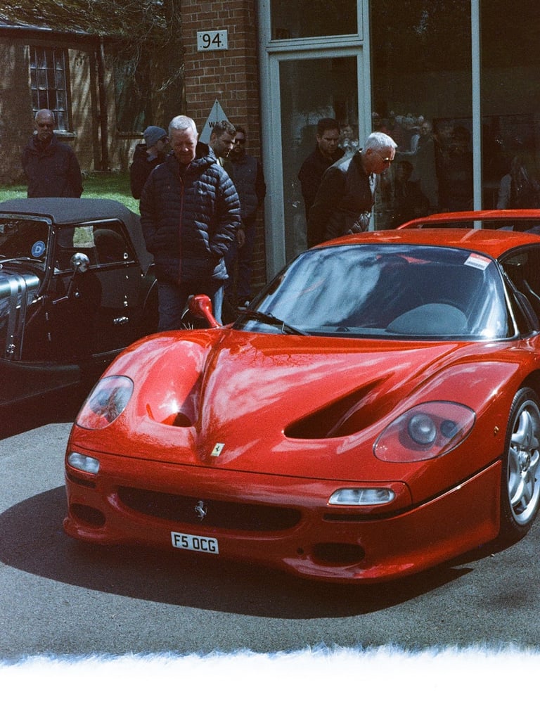 a red Ferrari F50 parked in front of a building, with a film burn at the bottom of the image