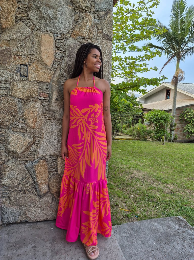 Mulher em pé usando um vestido com babado franzido, estampado nas cores rosa e laranja