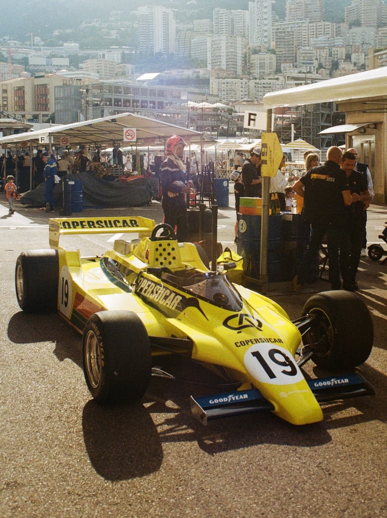 a yellow 80's Formula 1 car with a number of people standing around it